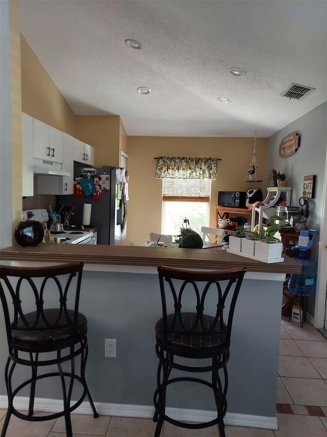 455 Eagle Dr, Kissimmee, FL 34759 - kitchen with a textured ceiling, white electric range oven, under cabinet range hood, white cabinetry, and a kitchen bar