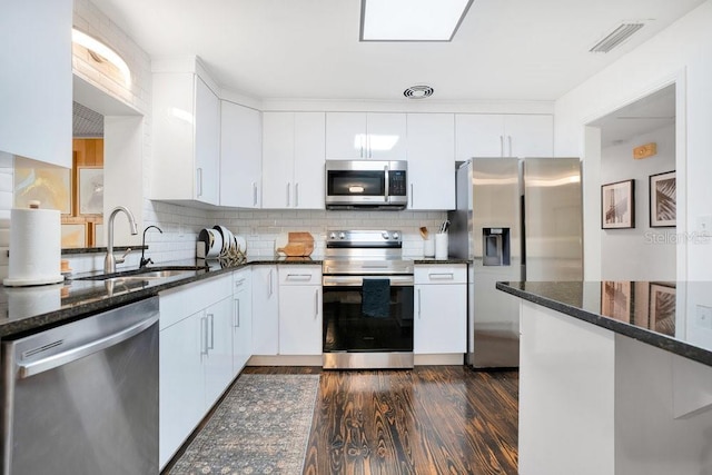312 Palencia Pl, Lakeland, FL 33803 - kitchen with stainless steel appliances, dark stone countertops, decorative backsplash, white cabinetry, and dark wood-style flooring