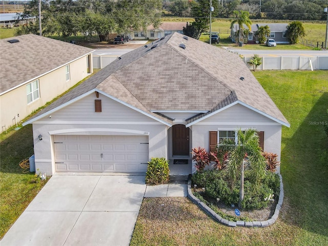 ranch-style home featuring a shingled roof, driveway, an attached garage, a front yard, and stucco siding