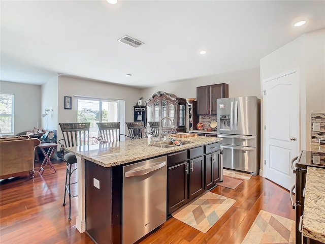 kitchen featuring appliances with stainless steel finishes, a sink, dark wood-style flooring, a center island with sink, and a breakfast bar area