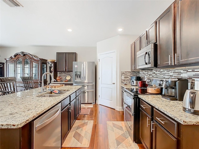 kitchen featuring stainless steel appliances, a sink, backsplash, light wood-style floors, and light stone counters
