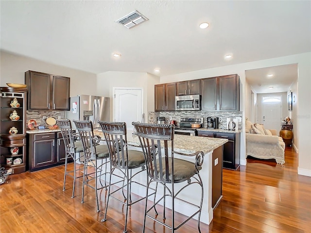 kitchen featuring appliances with stainless steel finishes, tasteful backsplash, a kitchen breakfast bar, wood finished floors, and recessed lighting