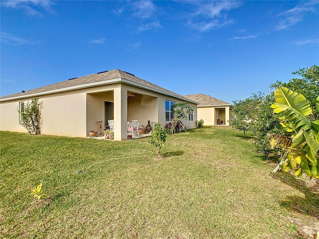 rear view of house featuring a lawn, stucco siding, and a patio