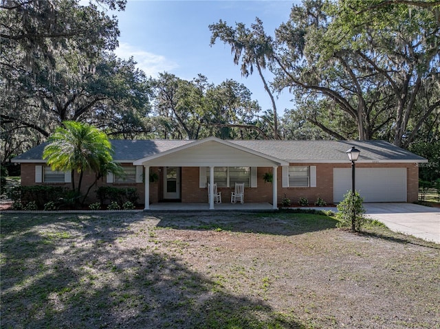 ranch-style home featuring driveway, brick siding, covered porch, and an attached garage