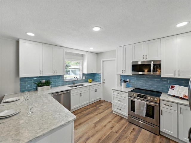 kitchen with stainless steel appliances, a sink, white cabinets, light wood-style floors, and decorative backsplash