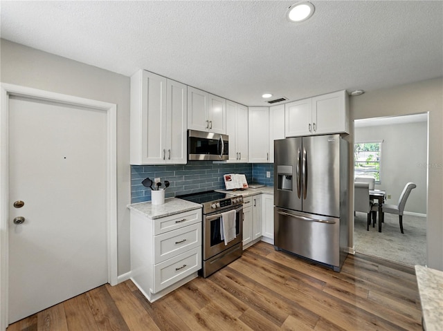 kitchen featuring appliances with stainless steel finishes, white cabinetry, decorative backsplash, wood finished floors, and a textured ceiling