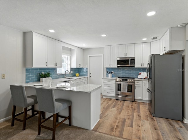 kitchen with stainless steel appliances, a peninsula, white cabinets, backsplash, and recessed lighting