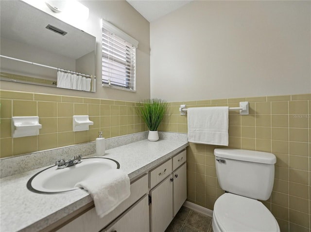 bathroom with toilet, tile walls, vanity, tile patterned floors, and wainscoting