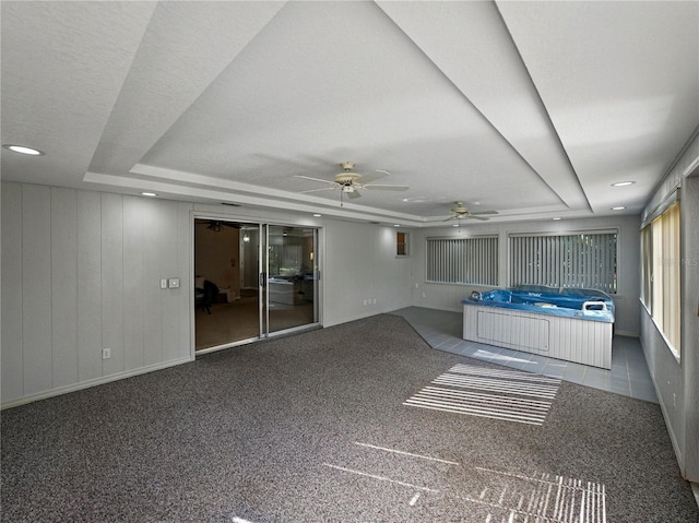 unfurnished living room featuring a raised ceiling, ceiling fan, carpet floors, and baseboards