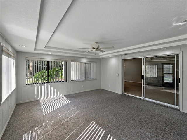 carpeted empty room featuring ceiling fan, a tray ceiling, a textured ceiling, and baseboards