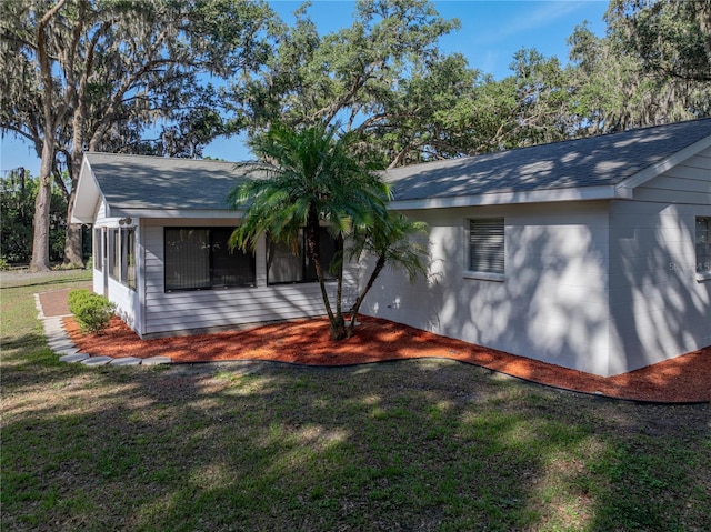 view of side of property featuring a yard, roof with shingles, and a sunroom