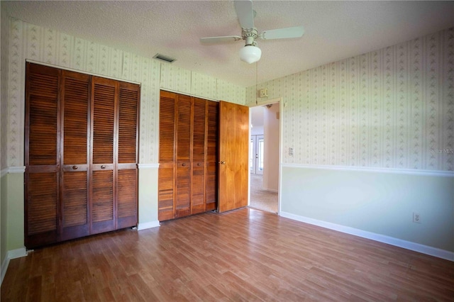 1920 Indian Trails Ct, Lakeland, FL 33813 - unfurnished bedroom featuring multiple closets, wood finished floors, wallpapered walls, a ceiling fan, and a textured ceiling