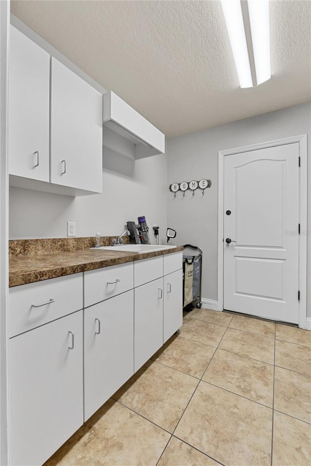 6542 Eagle Ridge Way, Lakeland, FL 33813 - kitchen with a textured ceiling, white cabinetry, dark countertops, light tile patterned floors, and a sink
