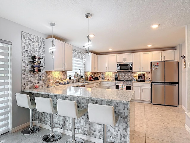 kitchen with appliances with stainless steel finishes, a peninsula, decorative backsplash, a sink, and baseboards