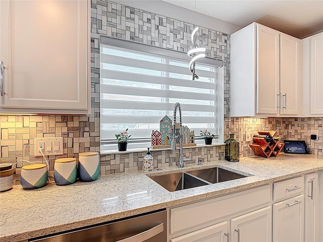 kitchen featuring a sink, stainless steel dishwasher, backsplash, white cabinets, and light stone countertops