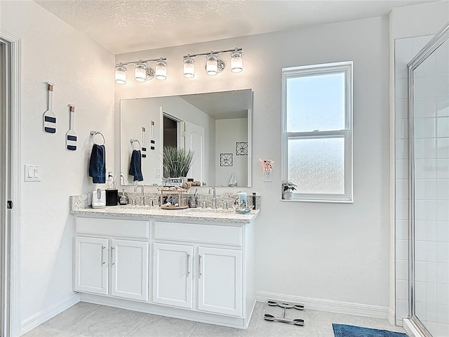 bathroom with double vanity, baseboards, tiled shower, tile patterned flooring, and a textured ceiling