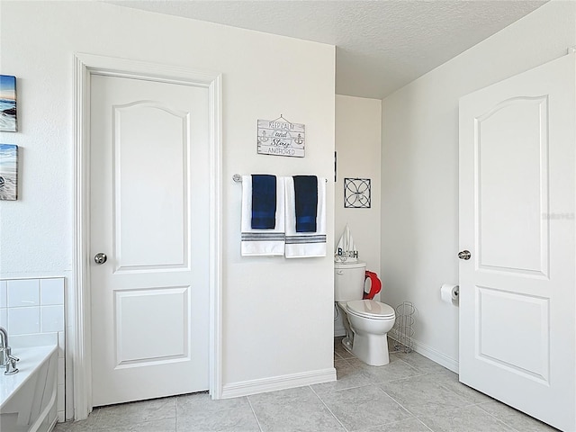 bathroom featuring a garden tub, baseboards, toilet, tile patterned flooring, and a textured ceiling