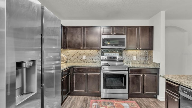 2293 Caspian Dr, Lakeland, FL 33805 - kitchen featuring stainless steel appliances, light wood-style floors, dark brown cabinets, light stone countertops, and backsplash
