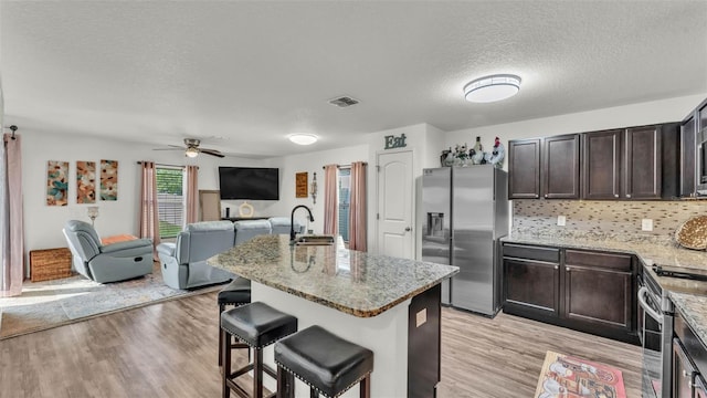 2293 Caspian Dr, Lakeland, FL 33805 - kitchen featuring stainless steel fridge with ice dispenser, a sink, a textured ceiling, light wood-type flooring, and a kitchen bar