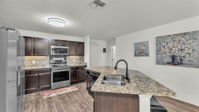 2293 Caspian Dr, Lakeland, FL 33805 - kitchen with appliances with stainless steel finishes, a sink, light wood-type flooring, a center island with sink, and dark brown cabinetry