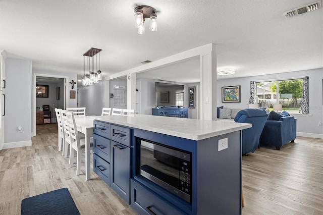 3810 Harrelson Rd, Lakeland, FL 33810 - kitchen featuring stainless steel microwave, blue cabinets, open floor plan, light wood finished floors, and a kitchen island