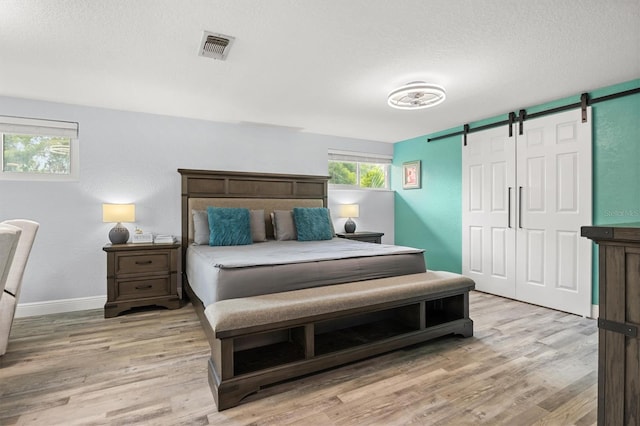 3810 Harrelson Rd, Lakeland, FL 33810 - bedroom featuring a barn door, light wood-type flooring, a textured ceiling, and baseboards