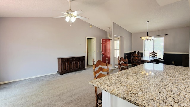 kitchen with a chandelier, a kitchen bar, ceiling fan, vaulted ceiling, and light stone countertops