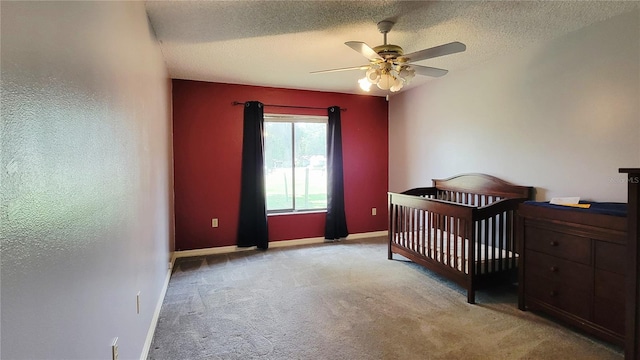 carpeted bedroom with a textured ceiling, baseboards, a ceiling fan, and a crib