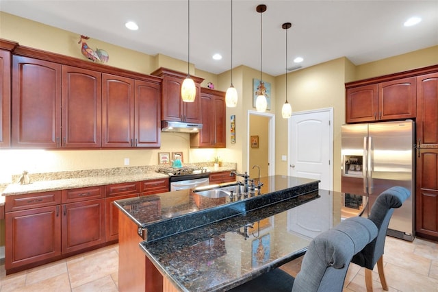 2731 Coventry Ave, Lakeland, FL 33803 - kitchen with stainless steel fridge, under cabinet range hood, reddish brown cabinets, a center island with sink, and decorative light fixtures