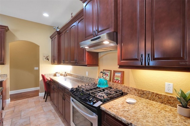 2731 Coventry Ave, Lakeland, FL 33803 - kitchen featuring under cabinet range hood, stainless steel gas range, arched walkways, baseboards, and light stone countertops