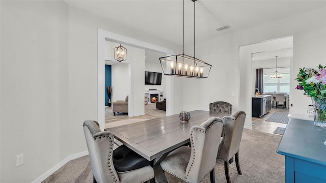 1146 Enclave Ct, Auburndale, FL 33823 - dining space with a chandelier, a warm lit fireplace, light colored carpet, and baseboards
