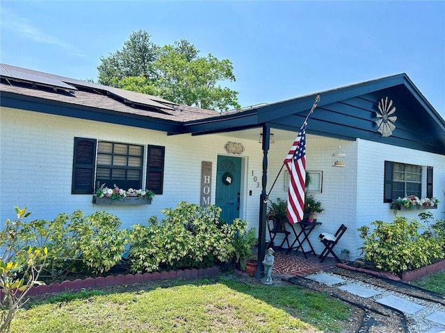 103 Inglis Way, Wauchula, FL 33873 - view of front of home featuring brick siding, covered porch, solar panels, a front lawn, and roof with shingles