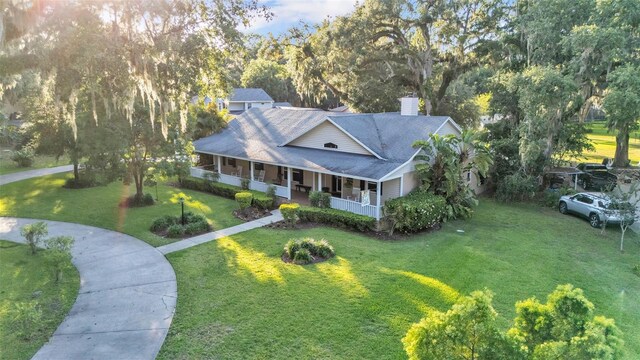 5108 Waterwood Dr, Bartow, FL 33830 - farmhouse inspired home with a porch, a front lawn, a chimney, roof with shingles, and view of wooded area