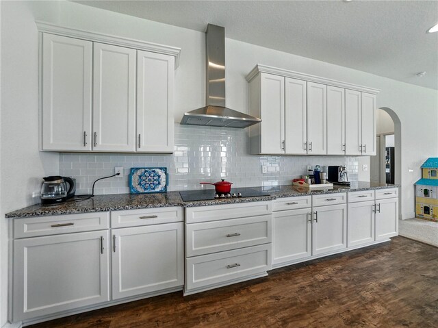 1547 Cordgrass Way, Lakeland, FL 33813 - kitchen featuring wall chimney range hood, black electric cooktop, arched walkways, dark stone counters, and a textured ceiling
