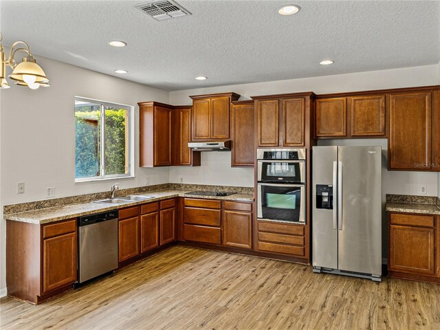 143 Alfani St, Davenport, FL 33896 - kitchen with appliances with stainless steel finishes, a sink, light wood finished floors, brown cabinetry, and a textured ceiling
