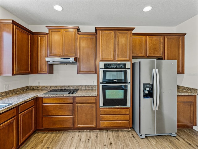 143 Alfani St, Davenport, FL 33896 - kitchen featuring appliances with stainless steel finishes, under cabinet range hood, light wood finished floors, brown cabinets, and a textured ceiling