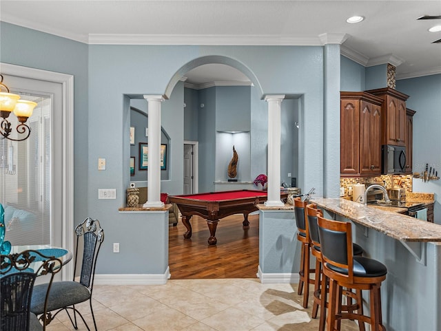 148 Melissa Trl, Auburndale, FL 33823 - kitchen featuring ornate columns, black microwave, ornamental molding, a kitchen breakfast bar, and light stone countertops
