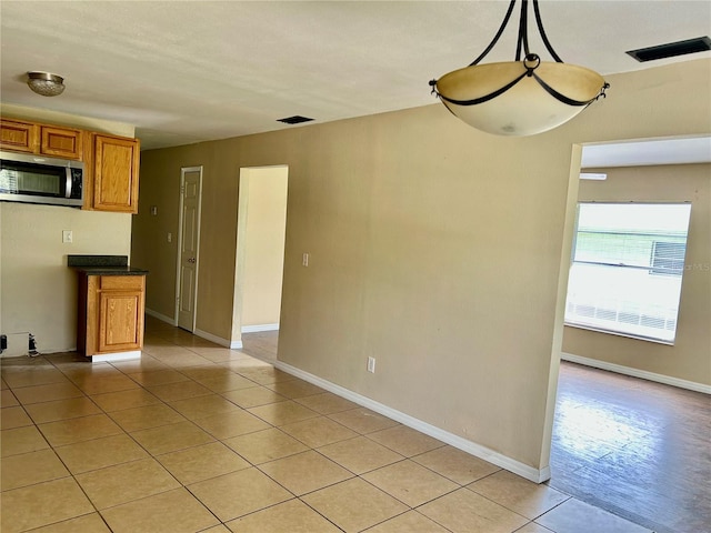 304 Bell St, Wauchula, FL 33873 - kitchen with stainless steel microwave, brown cabinets, light tile patterned flooring, dark countertops, and baseboards