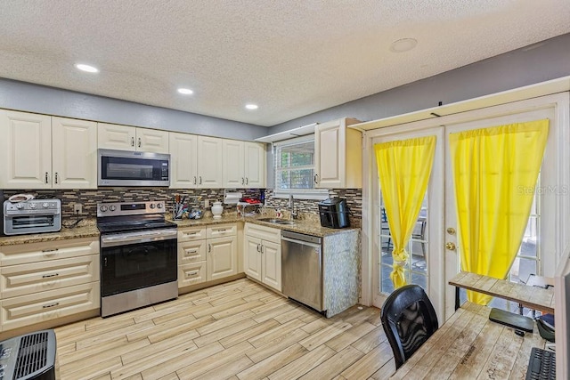 13411 Whitby Rd, Hudson, FL 34667 - kitchen featuring stainless steel appliances, a sink, a textured ceiling, decorative backsplash, and light wood-style floors