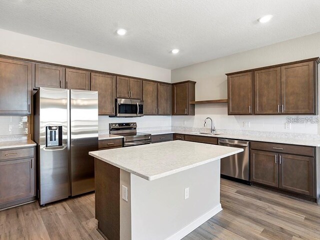 5771 Freshwater Canyon Dr, Saint Cloud, FL 34771 - kitchen featuring appliances with stainless steel finishes, a sink, dark brown cabinetry, light wood finished floors, and a center island