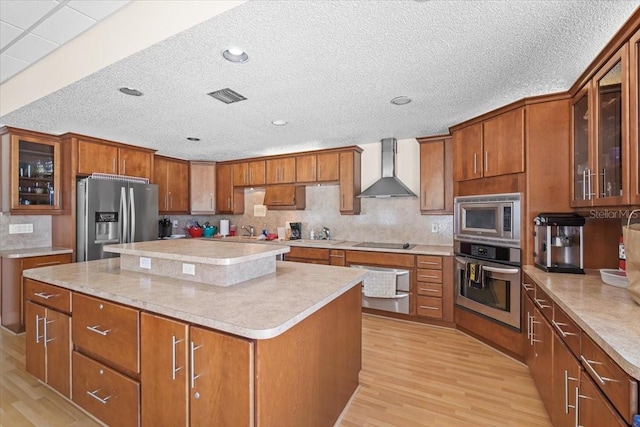 830 N Atlantic Ave Unit B502, Cocoa Beach, FL 32931 - kitchen featuring stainless steel appliances, wall chimney exhaust hood, brown cabinetry, light wood-style floors, and a textured ceiling