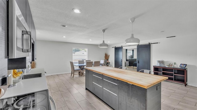934 Point View Ln, Lakeland, FL 33813 - kitchen featuring butcher block countertops, a barn door, gray cabinetry, decorative light fixtures, and a center island