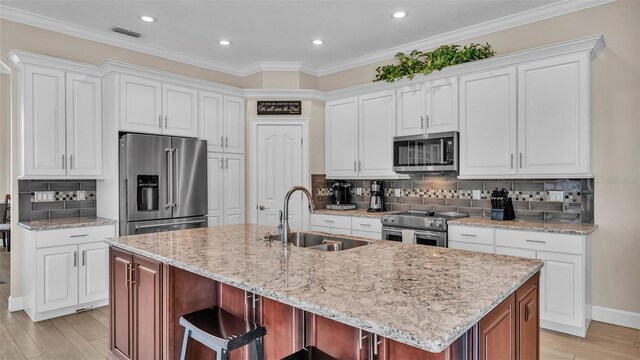 3121 Highlands By The Lake Way, Lakeland, FL 33812 - kitchen with stainless steel appliances, white cabinets, an island with sink, decorative backsplash, and light wood-style flooring