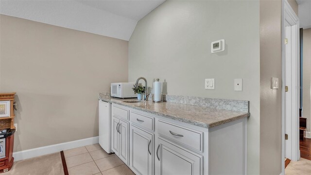 3121 Highlands By The Lake Way, Lakeland, FL 33812 - kitchen with white microwave, lofted ceiling, light tile patterned floors, white cabinetry, and light stone countertops