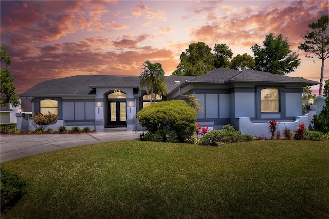 8721 Latham Ln, Hudson, FL 34667 - view of front of house featuring a lawn, stucco siding, a shingled roof, and french doors