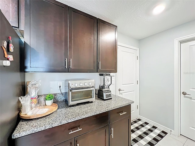 2929 Flying Blackbird Rd, Bartow, FL 33830 - kitchen featuring freestanding refrigerator, dark brown cabinetry, baseboards, light stone counters, and a textured ceiling
