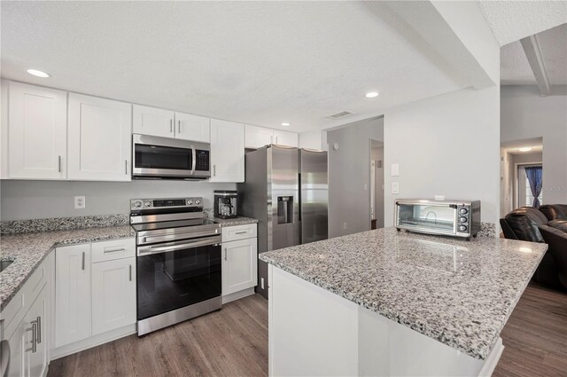 3080 Cross Fox Dr, Mulberry, FL 33860 - kitchen featuring stainless steel appliances, wood finished floors, white cabinets, light stone countertops, and a peninsula