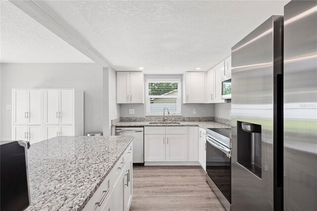 3080 Cross Fox Dr, Mulberry, FL 33860 - kitchen featuring appliances with stainless steel finishes, a sink, a textured ceiling, light wood-style floors, and light stone countertops