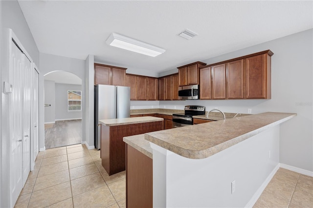 6819 Glenbrook Dr, Lakeland, FL 33811 - kitchen featuring appliances with stainless steel finishes, a kitchen island, arched walkways, light countertops, and a peninsula