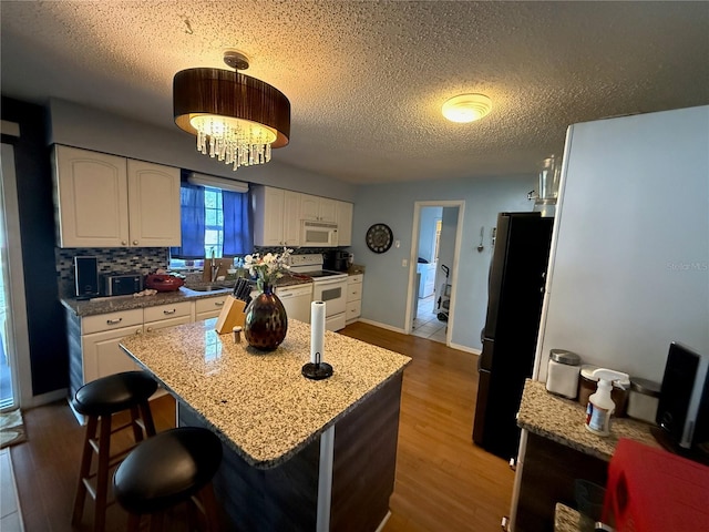 2424 Bates Ave SW, Winter Haven, FL 33880 - kitchen with white appliances, white cabinetry, wood finished floors, a textured ceiling, and a sink
